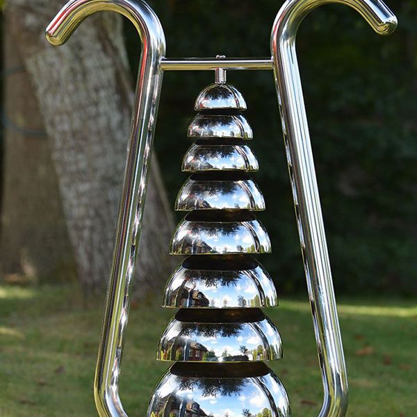 large shiny stainless steel outdoor musical instrument with a series of bells stacked on top of each other in a frame shaped like a lyre