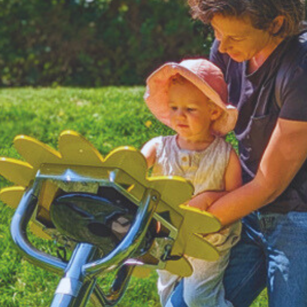 a lady holding a baby up and playing an outdoor musical instrument shaped like a sunflower