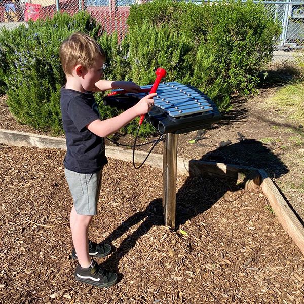 Young boy playing an outdoor xylophone in the new music garden at Morgan Autism Center