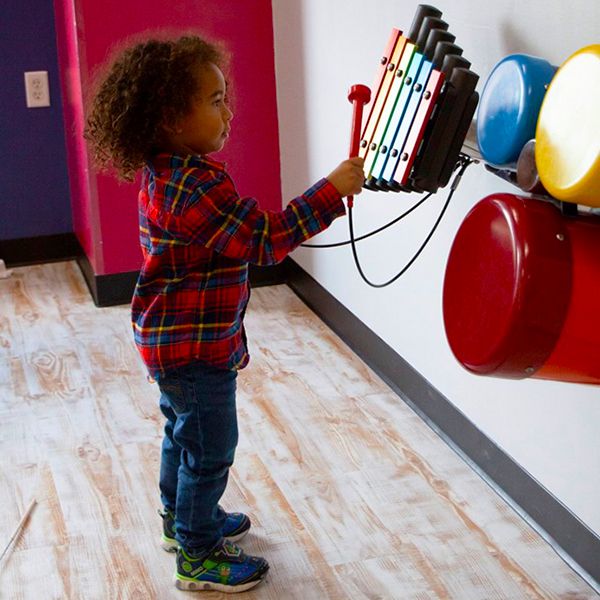 Young boy playing the rainbow xylophone fixed to the wall at the Building for kids children's museum