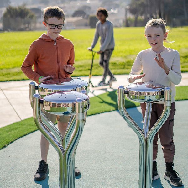 Two boys playing on three stainless steel outdoor tongue drums in McLaren PArk