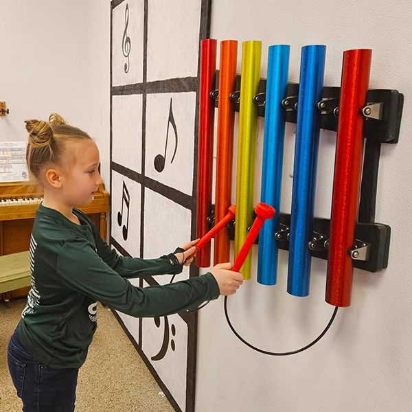 a girl playing a set of colourful musical chimes attached to a wall in the baraboo childrens museum