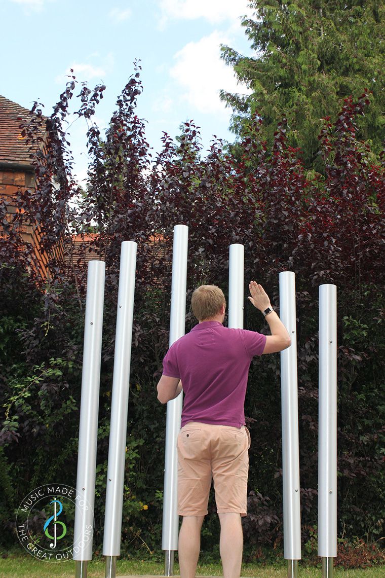 Man playing six large outdoor chimes with his hands