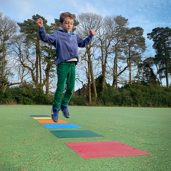 a young boy in a playground jumping onto colored squares that make a musical  tone when activated