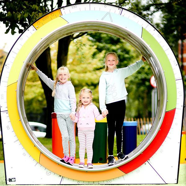 three young blond girls standing in a circular play structure in the inclusive music park in cathedral gardens, Belfast, Northern Ireland