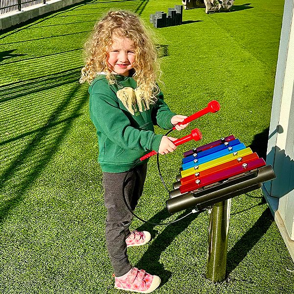 A young girl playing an outdoor metallophone in cross church preschool music garden