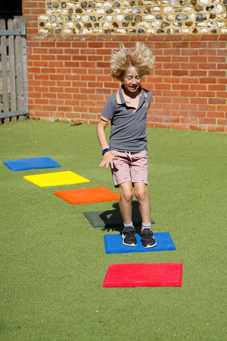 a young boy jumping on a set of six multicolored square 'pads' with hidden bells beneath them