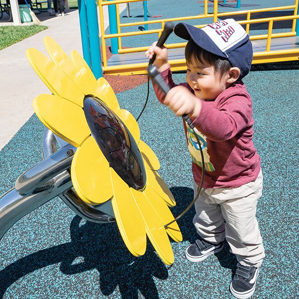 little boy in a cap hitting an playground drum shaped like a sunflower in an inclusive play park