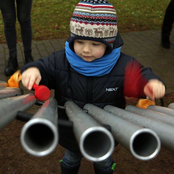 Little boy wearing a winter hat playing a large silver musical instrument in a park