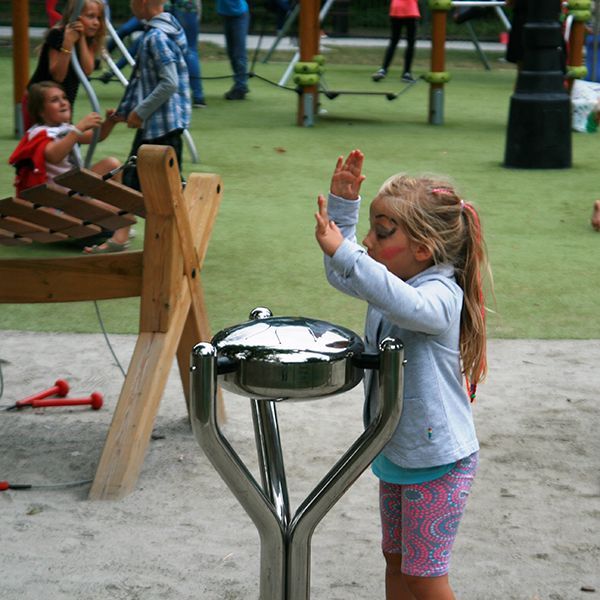 Young girl playing a silver steel tongue drum in a playground