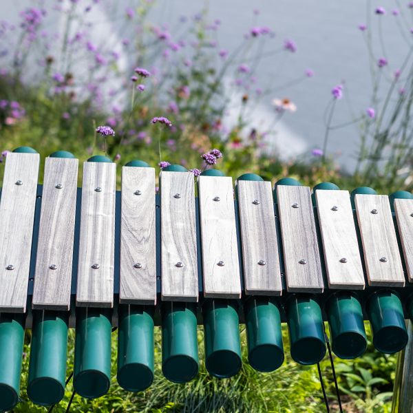 A large outdoor marimba with wooden notes and painted green resonators with flowers behind