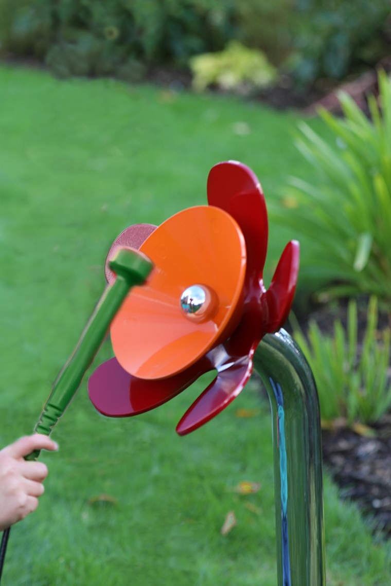 a young girl playing an orange and red musical flower outdoors in a sensory garden