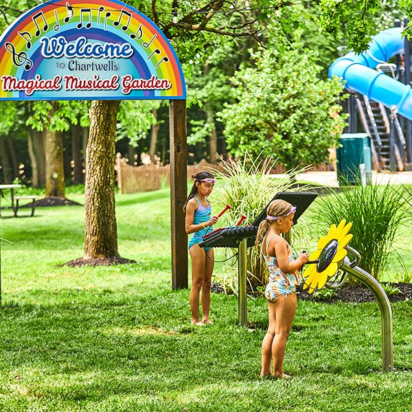 two girls in swimming costumes playing outdoor musical instruments in the Chartwell Happy Day Camp musical garden