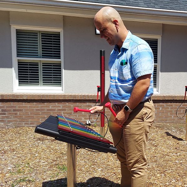 a man playing a rainbow colored outdoor xylophone in a church courtyard garden