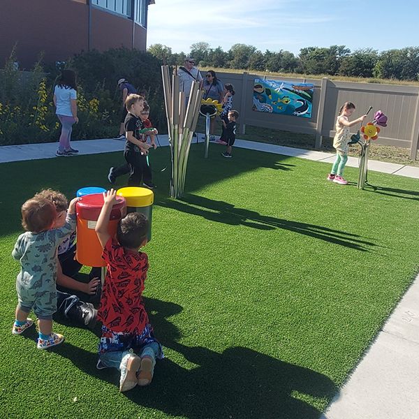 a group of young children playing on outdoor musical instruments on a lawn at the Kansas Wetlands Center