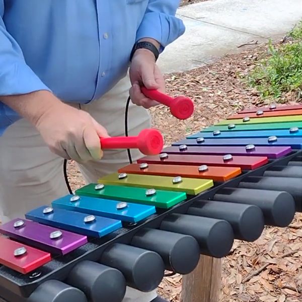 image showing the hands of someone playing a large outdoor rainbow colored xylophone