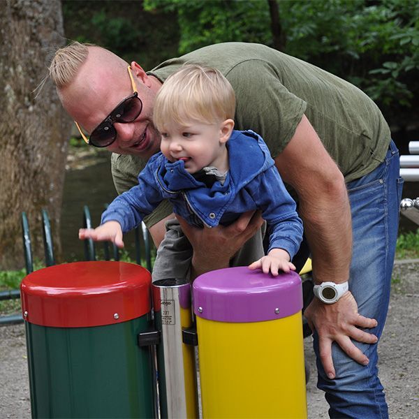 Man holding up a baby to play colourful conga drums in a park playground