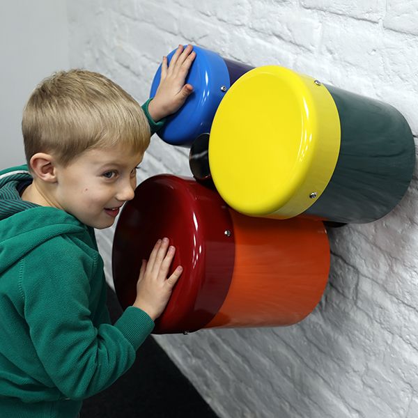 A group of three different sized wall mounted rainbow coloured outdoor bongo drums designed for smaller children