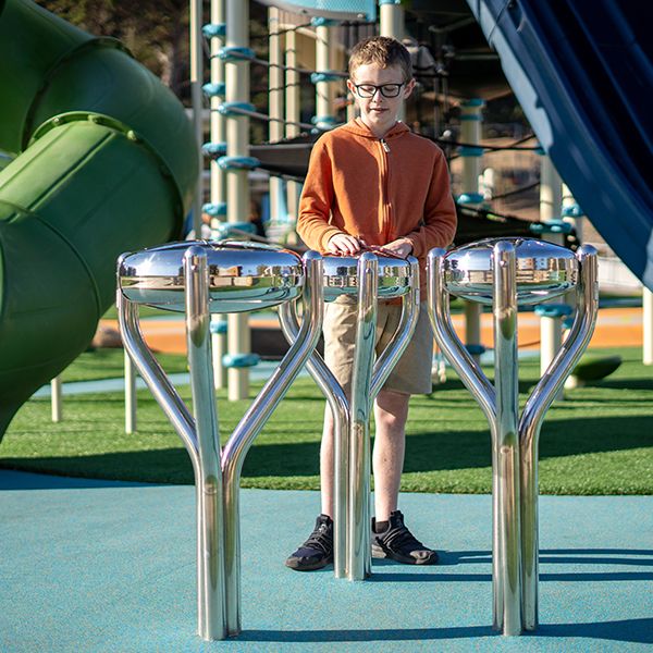 a boy playing a stainless steel tongue drum with a large slide behind him in McLaren Park