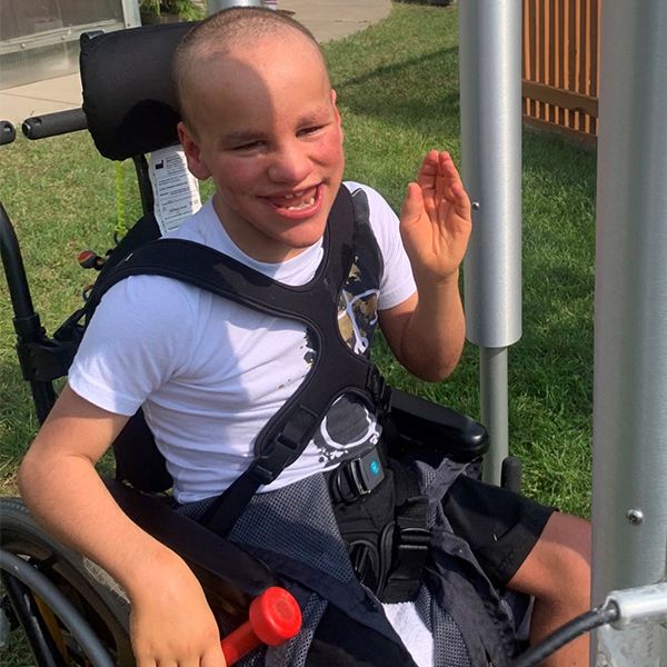 a young blind boy in a wheel chair playing tubular bell outdoor musical instruments in a music garden