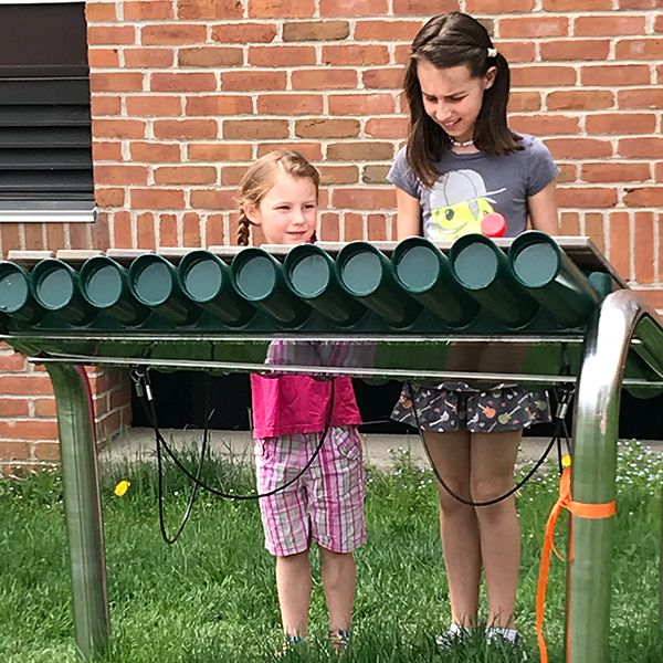 two girls playing the large outdoor marimba in the Dino Garden Liverpool Public Library New York