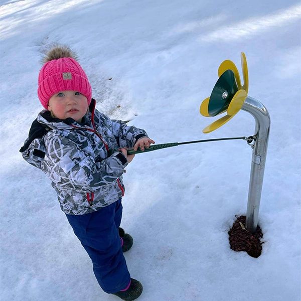 Little girl in snow gear playing an outdoor musical flower in the playground