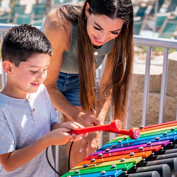 mother and child playing a rainbow colored outdoor xylophone in the sesame street music park at seaworld