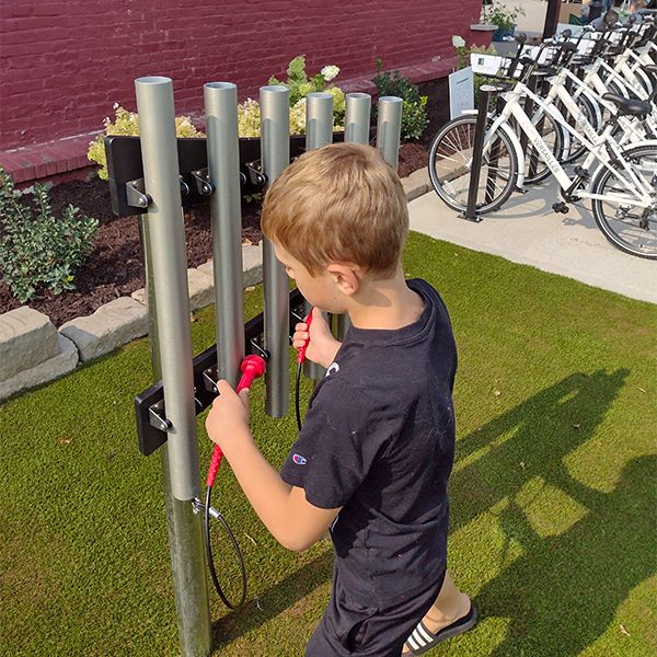 a young boy playing a set of outdoor musical chimes in the music garden at town of versailles