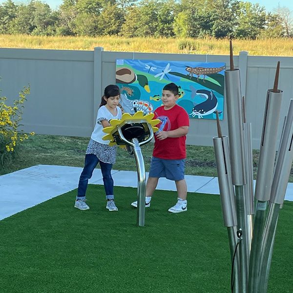 a young girl and boy playing an outdoor drum shaped like a large sunflower in the Kansas Wetlands Center new musical garden