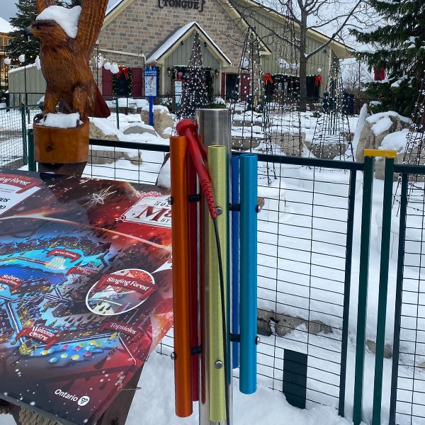 a rainbow colored chimes on a post in front of several unlit Christmas trees