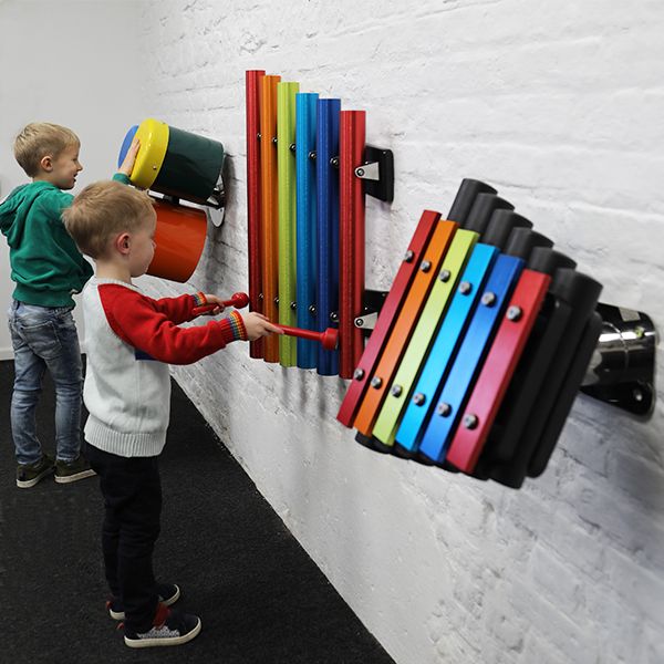 A collection of small rainbow coloured outdoor musical instruments mounted on the wall suitable for nursery or kindergarten aged children