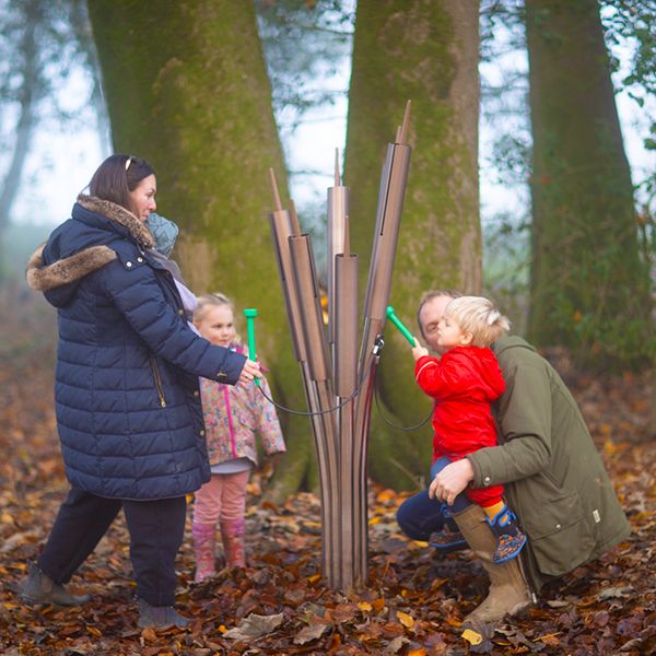 family of four playing an outdoor musical instrument shaped like catails