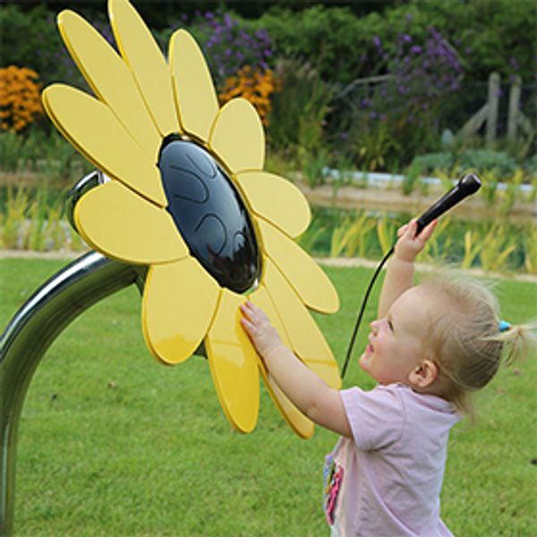 A young girl playing an outdoor musical drum in the shape and colours of a sunflower