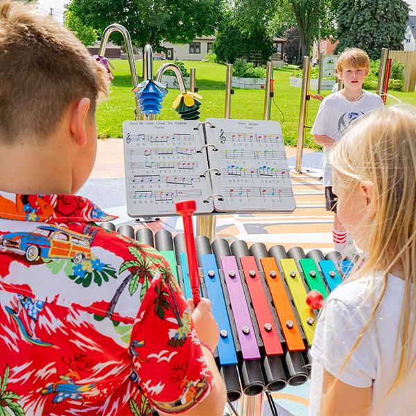 image of the back of a boy and girl playing a large outdoor xylophone with rainbow colored notes