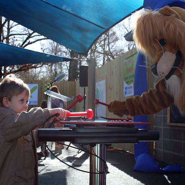 A little Boy playing an outdoor xylophone at little rock zoo with a person dressed as a lion