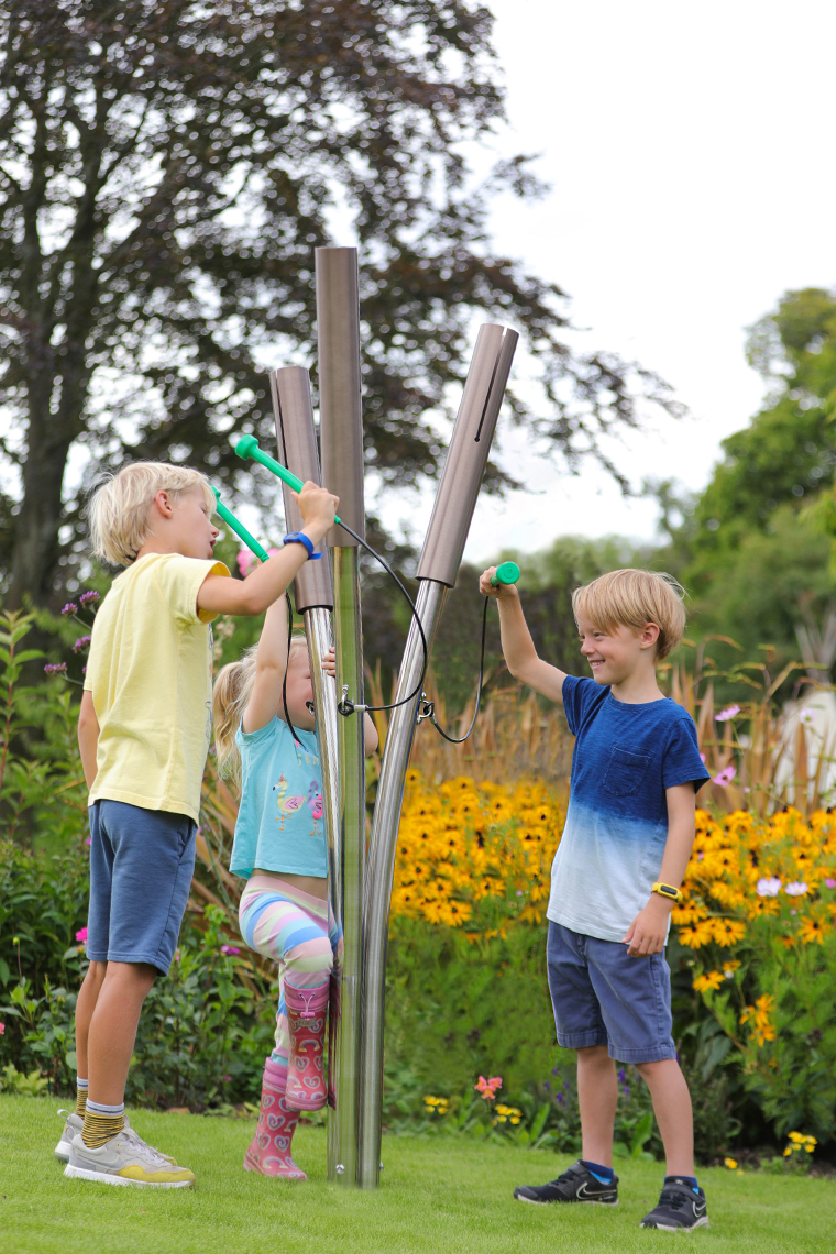 three children playing outdoor musical chimes shaped like cattails