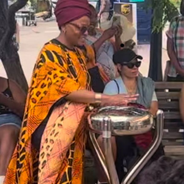 a lady of color wearing traditional african dress playing an outdoor tongue drum at the Dwight Baldwin memorial