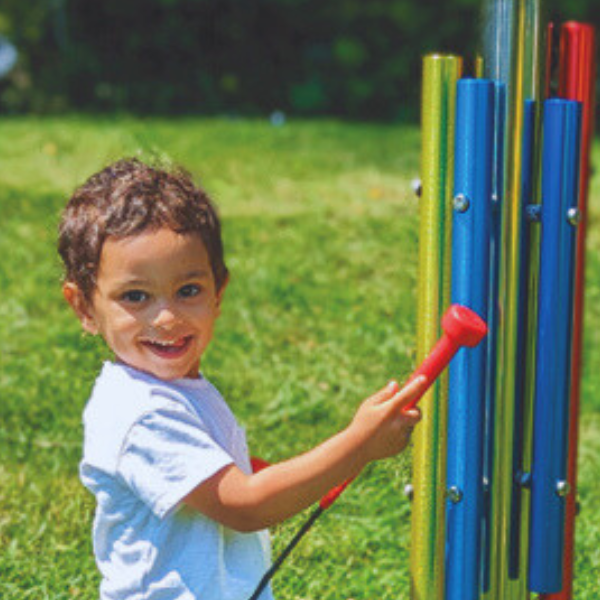 image of a young boyl playing colorful outdoor musical chimes in a library garden