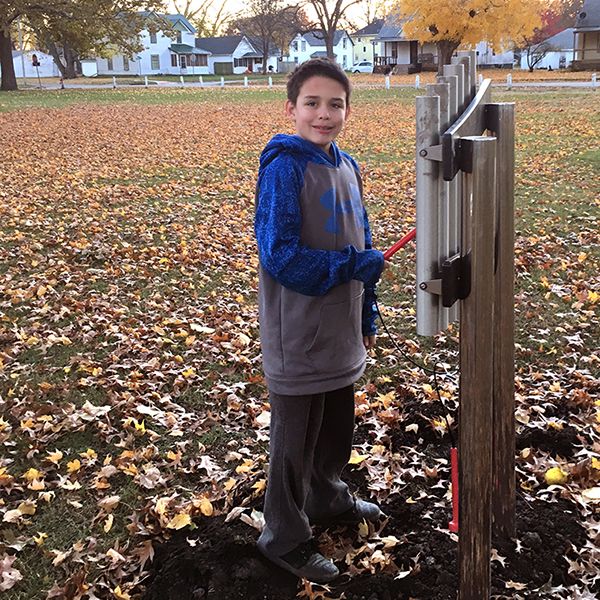 Teenage boy stood in a park in autumn playing outdoor musical chimes