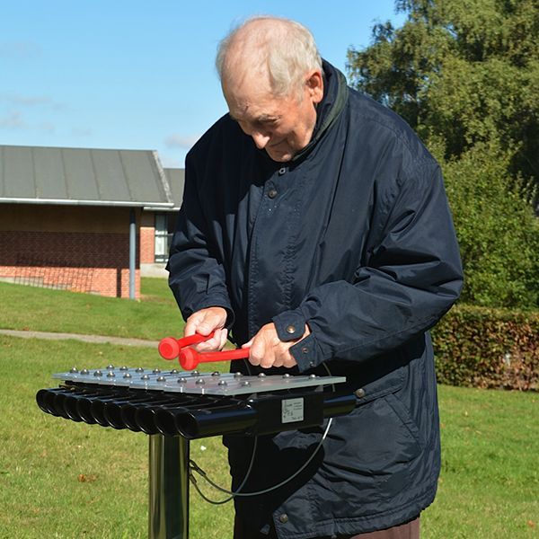 Elderly man smiling and playing on an outdoor xylophone in care home garden