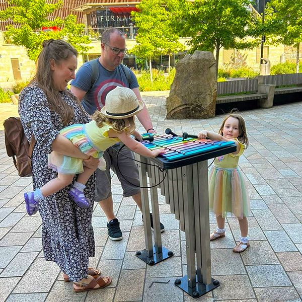 family playing on a outdoor xylophone with rainbow coloured notes in Sheffield city center music park