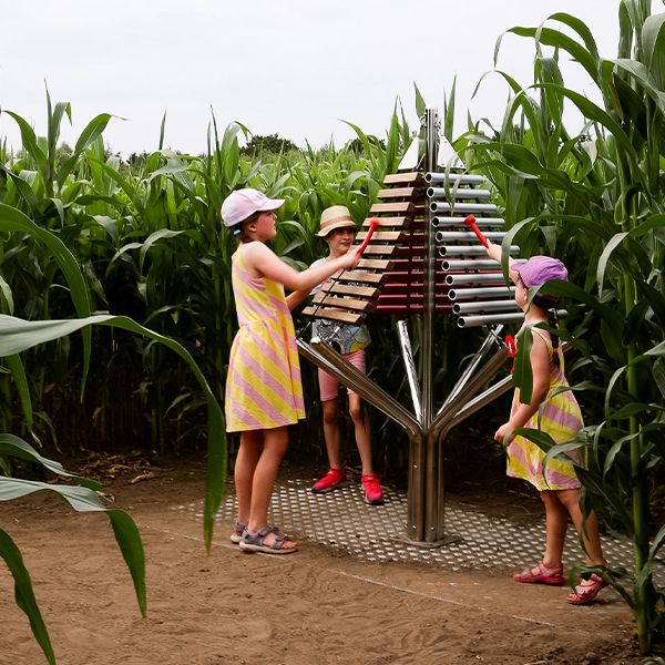 a three-sided outdoor xylophone being played by three girls standing in a corn field