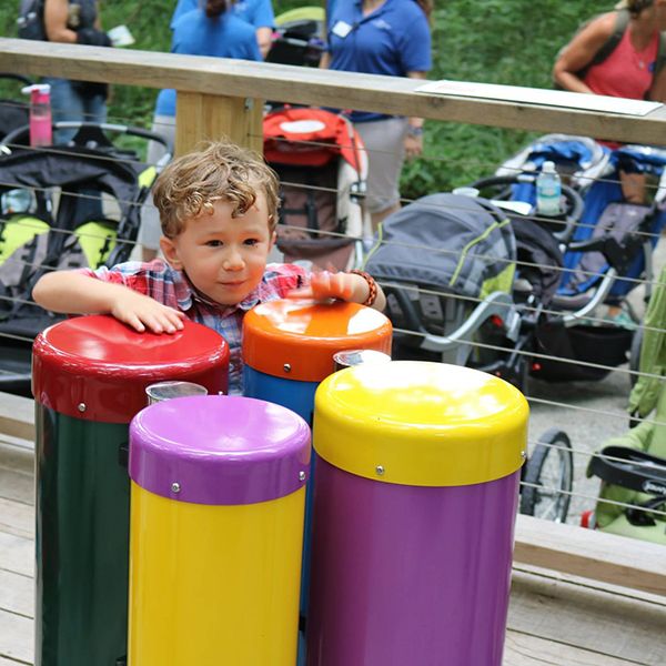 little boy playing the conga drums outdoor musical instruments at the Treetop Outpost at Conner Prairie History museum