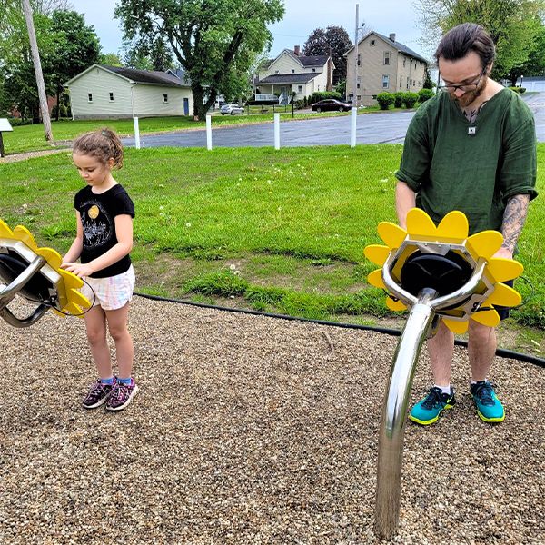 father and daughter playing large outdoor drums shaped like sunflowers on the hubbard library storywalk