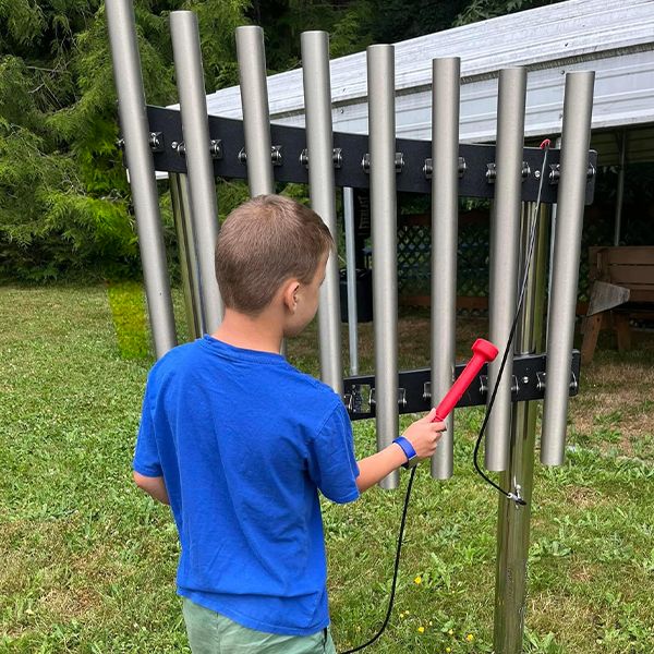 the back of a young boy playing silver outdoor musical chimes in the camp beausite new musical garden