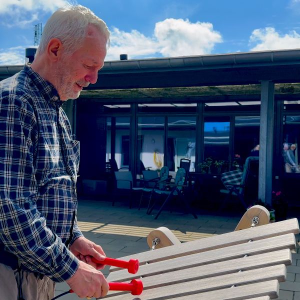 senior man playing a large outdoor wooden marimba xylophone with red mallets in a care home sensory garden