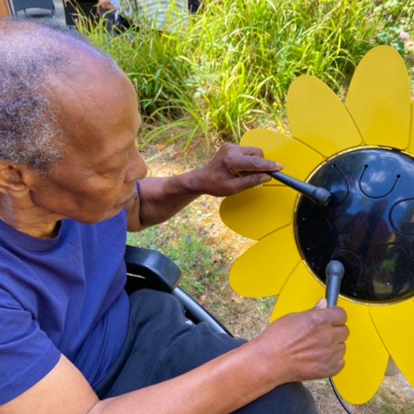 an older man in a wheelchair playing an outdoor drum shaped like a sunflower.