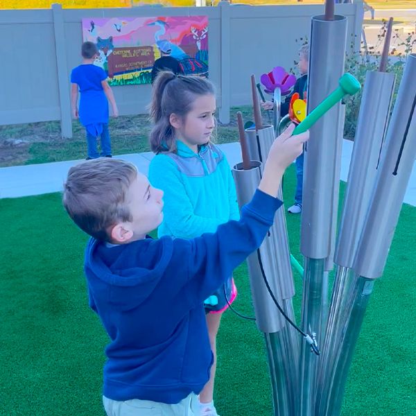 two children playing an outdoor musical instrument made to look like cattails in the Kansas Wetlands Center new musical garden