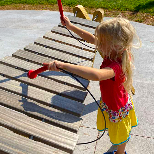 a close up image of a young girl playing a large outdoor musical marimba in a music playground