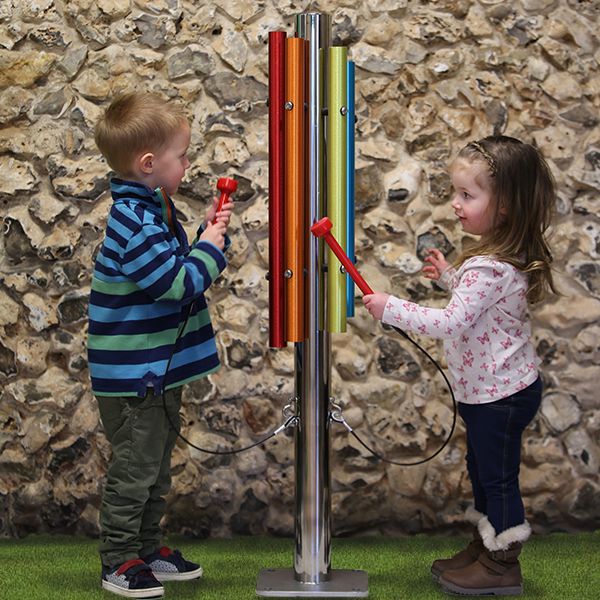 A little boy and girl playing an outdoor musical instrument made of a single stainless steel post and five bright coloured chimes attached